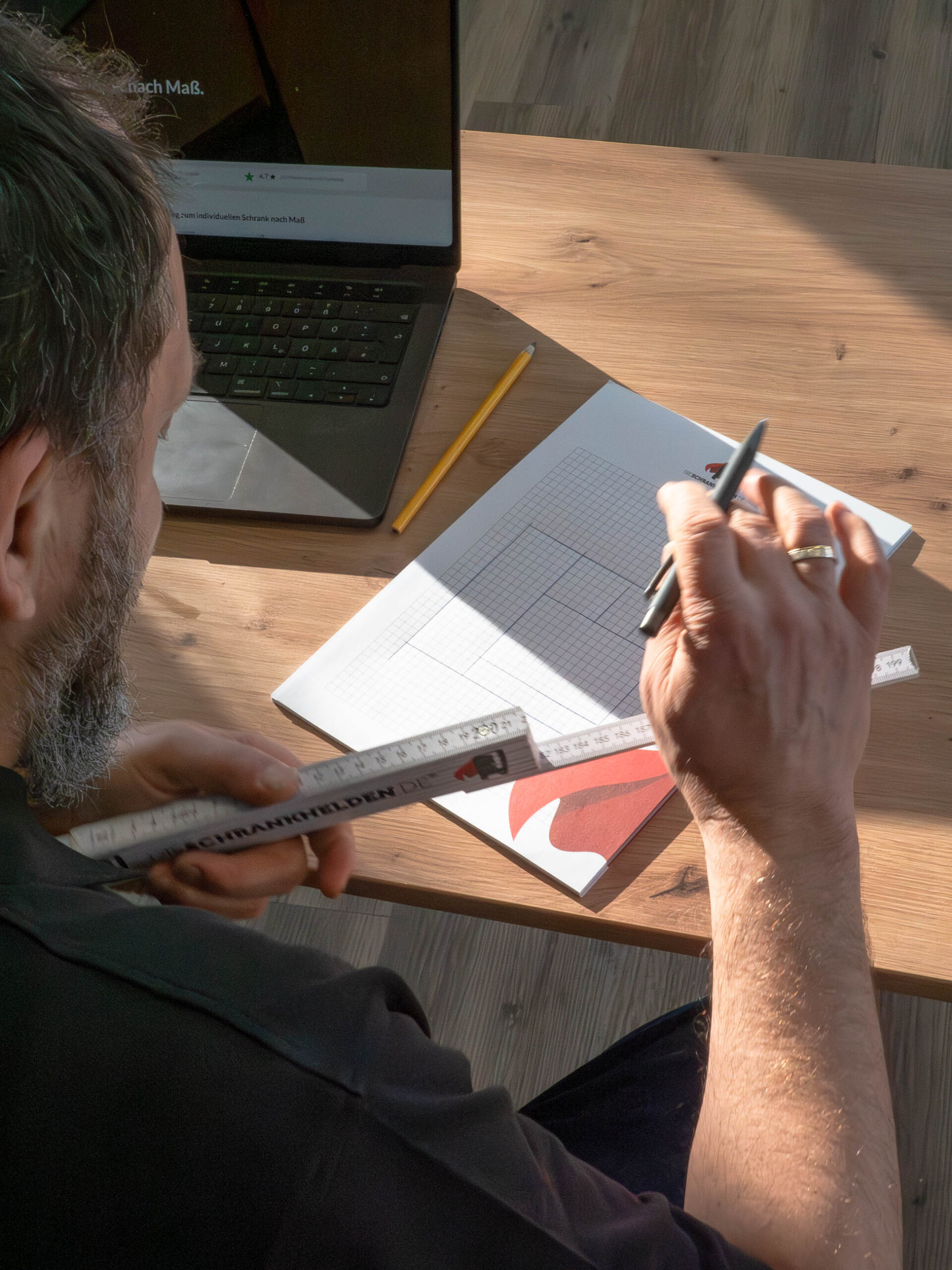 Carpenter plans custom-made cabinet with sketch, tape measure and laptop at the table
