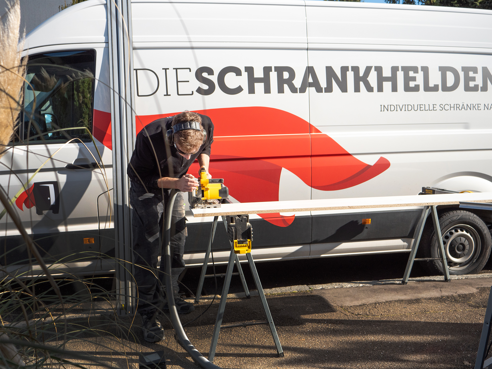 Carpenter processes wooden panel on site with machine in front of a Cabinetheroes van