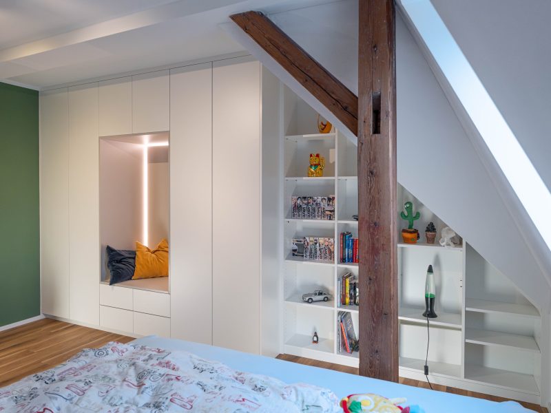 Sloping ceiling cabinet in matt white with light gray inlay behind wooden posts