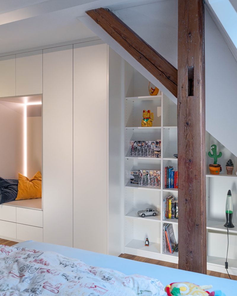Sloping ceiling cabinet in matt white with light gray inlay behind wooden posts