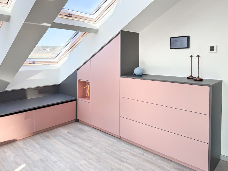 Custom-made cabinet for under-eaves and sloped ceilings with antique rose-colored fronts, anthracite accents, and handle-less drawers.