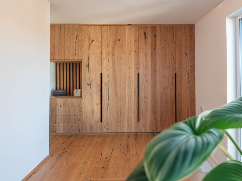 A wall-to-wall, custom-built built-in cabinet made of rustic oak with long black handles, drawers, and an open niche.