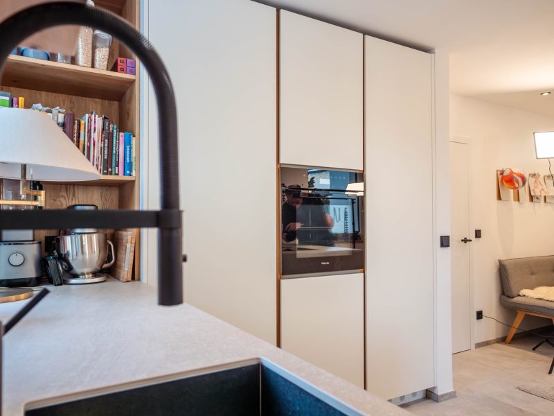 Modern custom kitchen with white handle-less cabinet fronts, wood accents, a built-in oven, and open shelving.